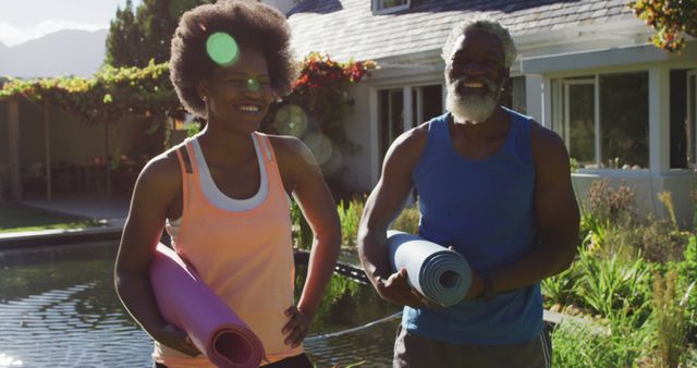 African american senior couple exercising outdoors carrying yoga mats in sunny garden. staying at home in isolation during quarantine lockdown.
