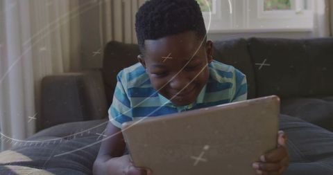 Smiling boy using tablet while relaxing on dark sofa with sunlight streaming through window