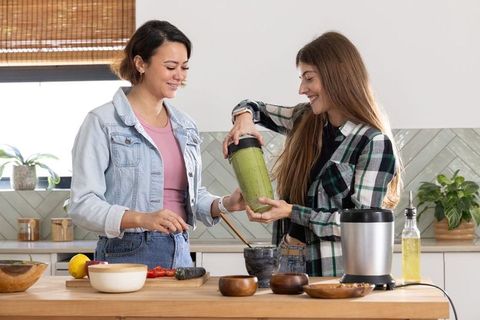 Pouring green smoothie from blender cup into mortar by diverse friends in modern kitchen