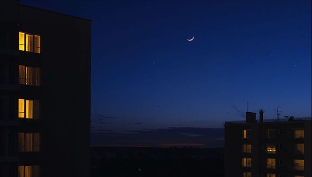 Crescent moon hovering over dusk city skyline with warm high-rise window glow