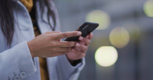 This stock photo captures a woman texting on her smartphone in an outdoor urban area. Ideal for representing modern communication, connectivity, social media interactions, and mobile technology usage in cities. Can be used in blog posts, articles, websites, and marketing materials focused on technology, urban living, telecommunications, and lifestyle.