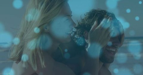 Couple Sharing Playful Piggyback at Sunny Beach with Blue Bokeh Lights