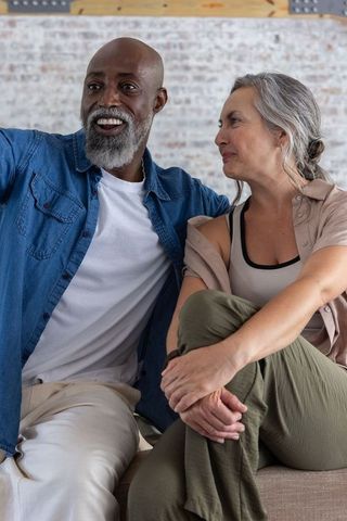 Senior interracial couple relaxing and conversing on loft sofa by painted brick wall