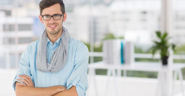 The young professional man is standing confidently with his arms crossed in a modern office. This image is perfect for portraying professionalism, confidence, and modern business settings. Ideal for use in corporate websites, business presentations, marketing materials, and career-oriented content.