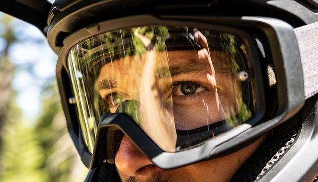Closeup of mountain biker wearing full-face helmet with clear goggles reflecting forest