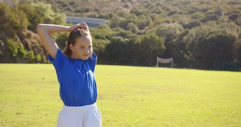 Young Girl Warming Up on School Field Under Sunny Sky