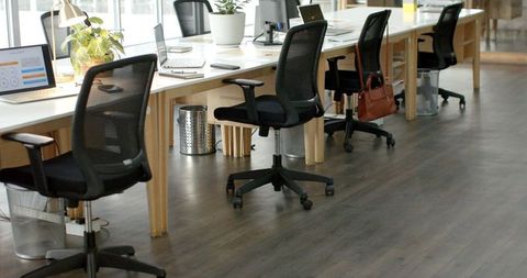 Minimalist open-plan coworking workspace featuring black mesh swivel chairs and long light-wood desk