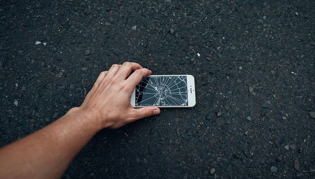 Reaching hand touching cracked smartphone on asphalt closeup of shattered screen