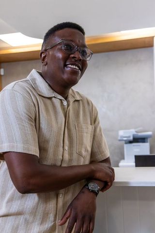 African american man leaning on reception counter smiling in beige shirt and glasses
