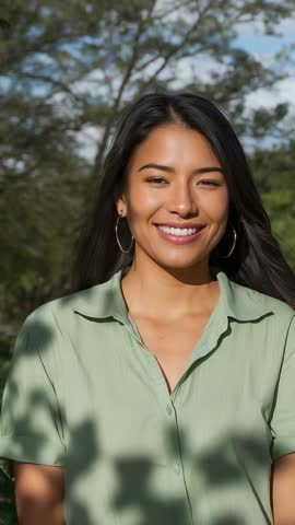 Smiling woman under tree with dappled sunlight and breeze rustling leaves vertical video