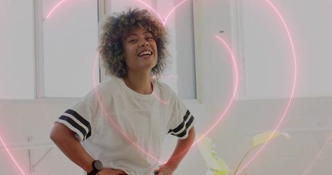 Smiling woman laughing in casual striped tee with neon heart overlay, energetic studio