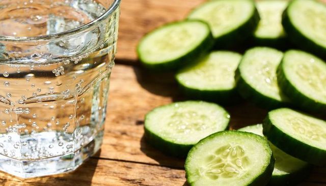 Glinting glass holding sparkling water with sliced cucumber on sunlit wooden tabletop