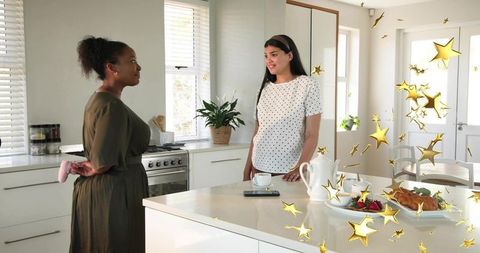 Two women talking over breakfast at modern kitchen island with teapot and croissant