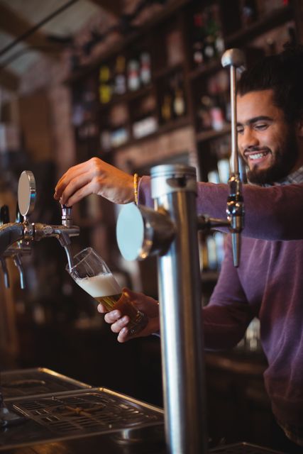 Bartender pouring beer from a tap at a bar counter, smiling while serving a draft beer. Ideal for use in articles or advertisements related to nightlife, hospitality industry, bars, pubs, and beverage services.