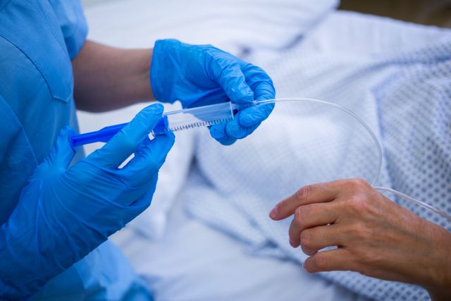 Nurse wearing blue gloves administering an injection to a patient in a hospital setting. Useful for illustrating healthcare, medical procedures, patient care, and hospital environments. Ideal for medical articles, healthcare websites, and educational materials.