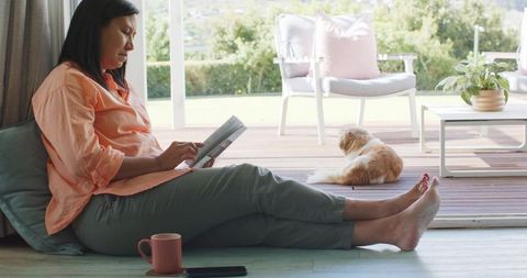 Relaxing on sunlit floor reading novel with cat lounging on deck