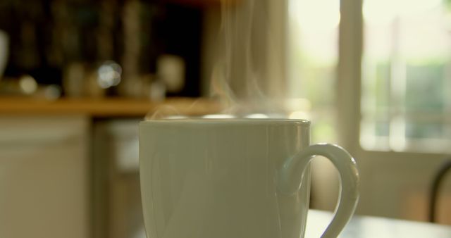 Steaming mug of coffee on kitchen table, ideal for illustrating morning routines, cozy home settings, or breakfast-themed content. Perfect for blogs, social media posts related to comfort, warm beverages, food photography, or lifestyle.