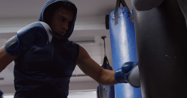 This depicts a young boxer training with a heavy bag in a gym, showcasing intense focus and determination. Ideal for use in fitness promotions, sports training materials, and motivational content.