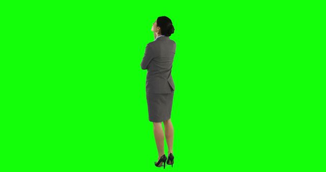 Businesswoman stands with arms crossed, viewed from behind. She wears a formal suit and stands against a green screen background, which allows easy insertion into various presentations, marketing materials, or advertisements. This is useful for projects related to business, professional attire, backgrounds removal, or corporate settings.