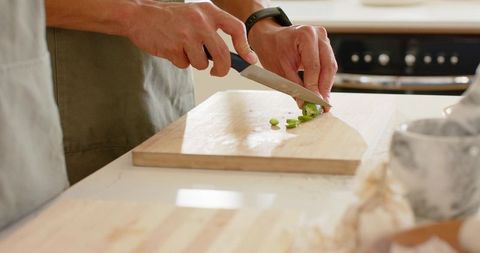 Couple chopping scallions on wooden cutting board with chef knife and wristwatch
