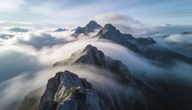 Aerial jagged alpine ridge rising through rolling mist and clouds at dawn, dramatic peaks