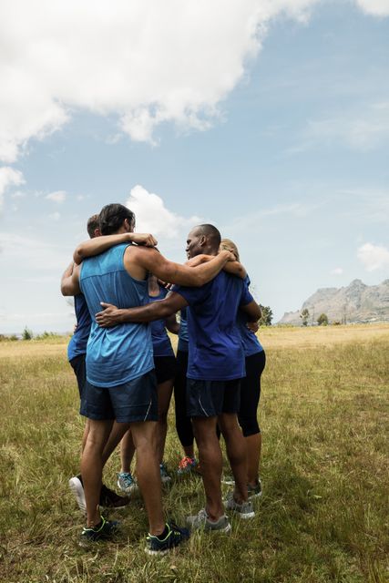 Group of fit individuals forming a huddle during an outdoor bootcamp. Ideal for promoting teamwork, fitness programs, group exercise classes, and motivational content related to physical fitness and healthy lifestyles.