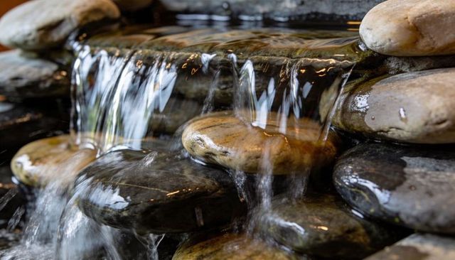 Flowing water cascading over stacked river stones with glossy reflections for tranquil garden design