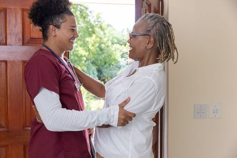 Home nurse embracing senior african american woman at doorway providing compassionate care