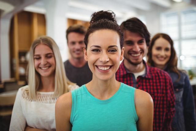 Group of young professionals smiling and standing together in a modern office environment. Ideal for use in business websites, team-building promotions, and workplace culture materials.