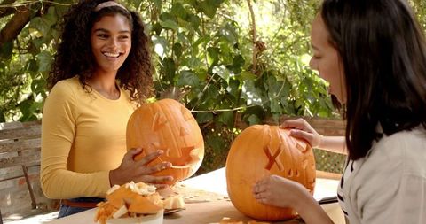 Multiracial female friends smiling while carving pumpkins outdoors