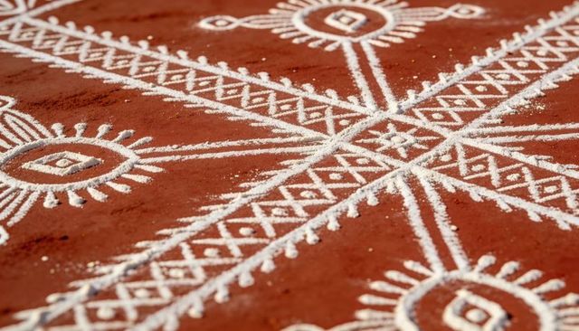 White powder rangoli on terracotta floor — geometric kolam with sunburst cross lattice