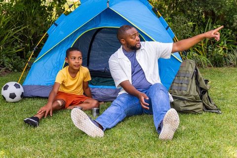 African american father and son backyard camping with blue tent pointing toward adventure