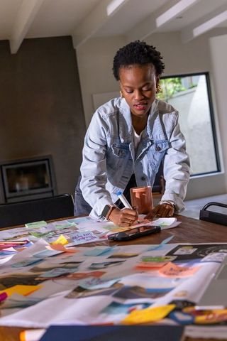 African american woman leaning over table, creating moodboard with sticky notes