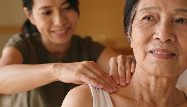 Senior woman receiving shoulder massage from caregiver, warm in-home care closeup
