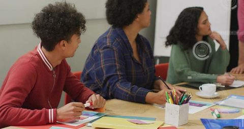 Young team collaborating in creative workshop around wooden table with colorful supplies