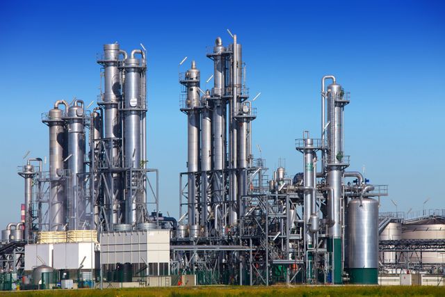 Oil refinery with tall metal towers and extensive piping under clear blue sky, ideal for illustrating energy production, petrochemical industry, or industrial engineering themes. Useful for educational materials about fuel production, industry reports, company brochures, or energy sector advertisements.