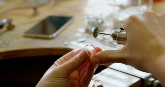 Jeweler using rotary tool for polishing gold ring, showcasing craftsmanship and detailed metalwork in workshop. Can be used for illustrating artisanal jewelry making processes, promoting handmade jewelry brands, or highlighting skills in craftsmanship and design industries.