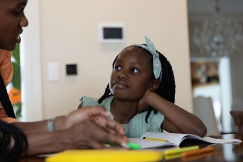African american mother guiding daughter through homework at kitchen table, studying together