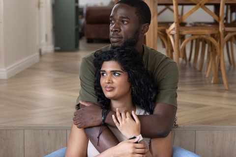 Interracial couple embracing on wooden steps in cozy open-plan living room with smartwatch