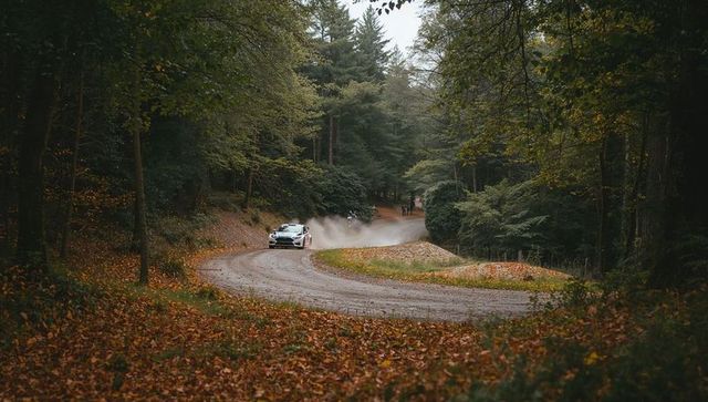Rally car kicking up dust in autumn forest