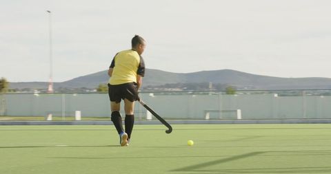 Female field hockey player dribbling ball on turf stadium
