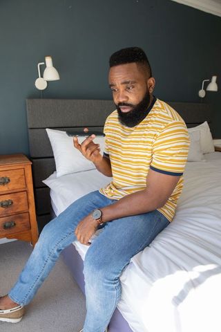 Relaxed man checking smartphone while seated on bed