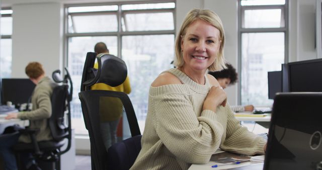 Portrait of smiling caucasian creative businesswoman sitting by desk in modern office. business and office work environment.