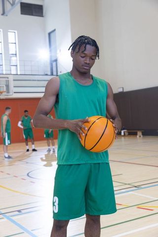 African american basketball player holding ball on indoor court in green jersey number 3
