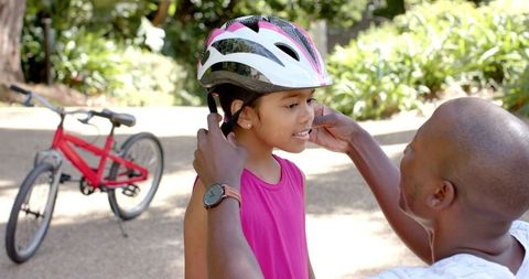 Father adjusting daughter's helmet before bike ride