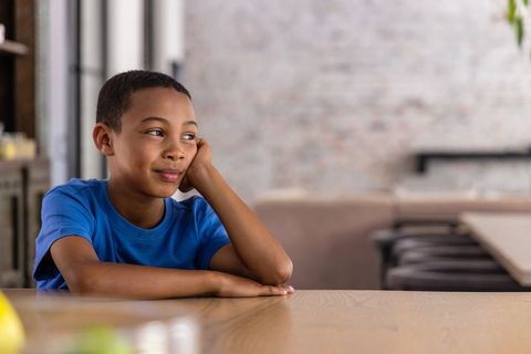 African american boy daydreaming at wooden table in bright modern living space