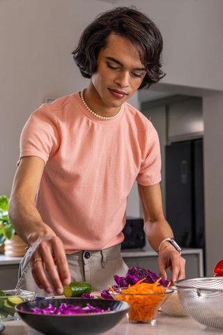 Indian man preparing healthy colorful salad at kitchen counter arranging shredded cabbage