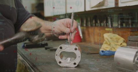 Mechanic shaping metal housing with punch and hammer on workbench with digital code overlay
