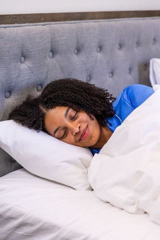 African american woman sleeping peacefully in blue satin pajamas on white duvet
