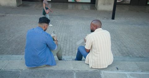 Two friends sitting on city steps sharing takeout and iced drinks, casual outdoor break